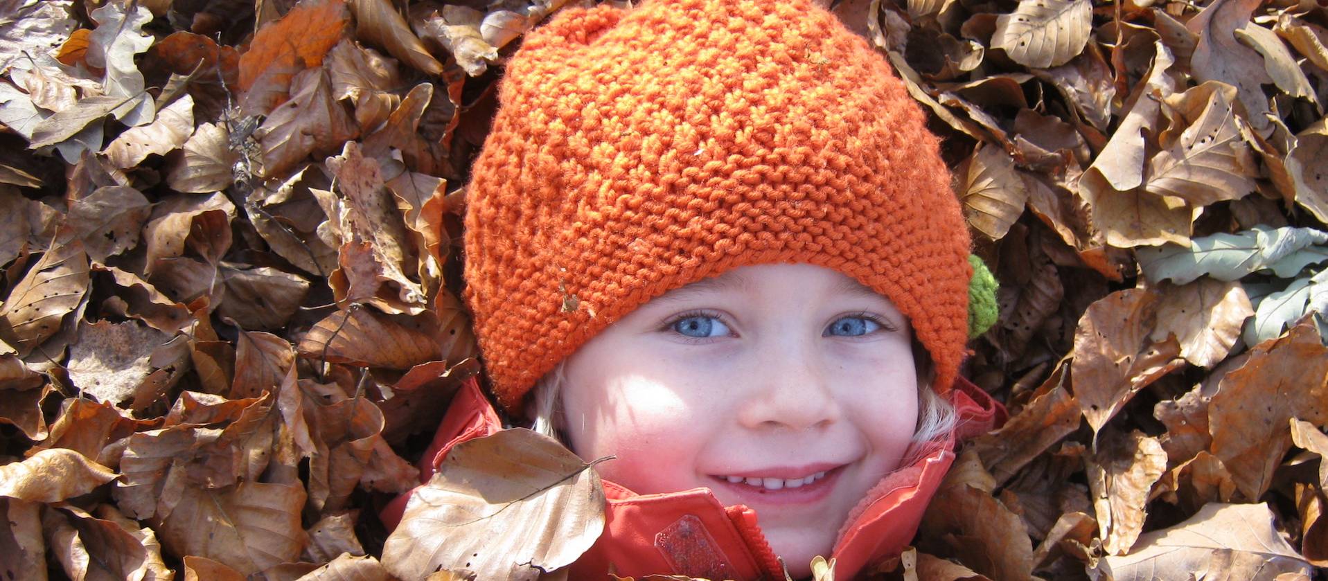 Kind versteckt sich unter Herbstlaub
